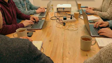 Personen tippen auf Laptops bei Besprechung.