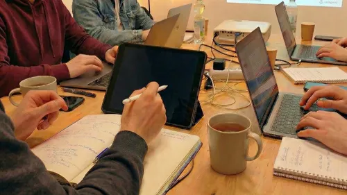 Menschen arbeiten mit Laptops und Notizbüchern am Tisch.