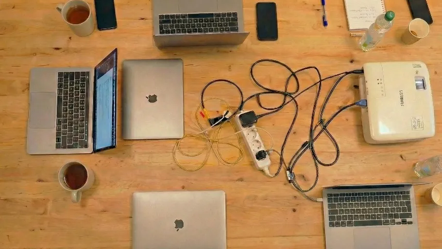 Laptops, cables, and mugs on a wooden table.