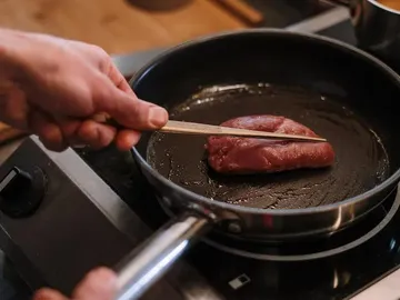 Ein Stück Fleisch wird in einer Pfanne umgedreht.
