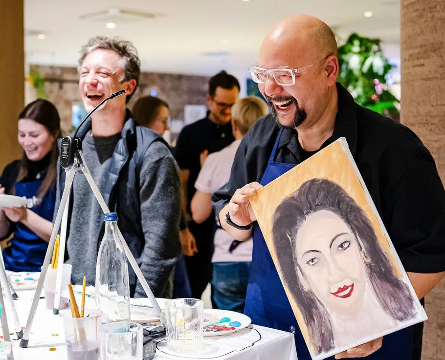 People laughing and holding a portrait painting.