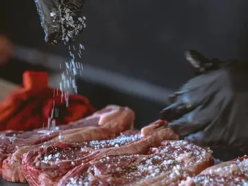 Rohe Steaks werden mit Salz bestreut, in einer Küche.