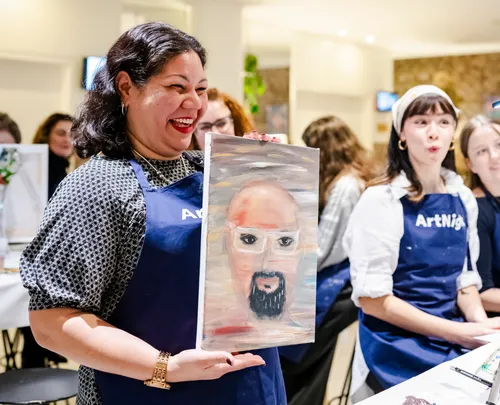 Woman joyfully displaying her painting at event.
