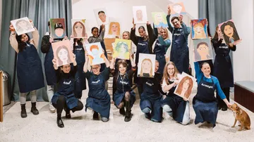 Group holding portrait paintings in room.