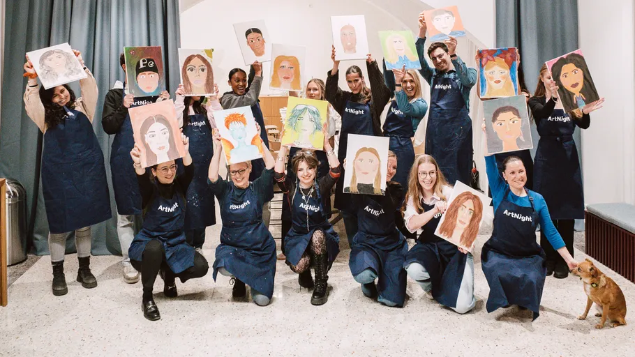 Group holding portrait paintings in room.