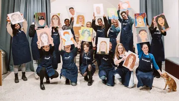 Group displaying painted portraits in art studio.