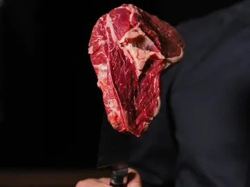 Fleischstück wird mit einem Messer in dunklem Raum gehalten.
