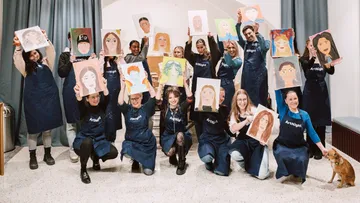 Group holding portraits, wearing aprons, indoors.