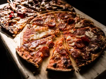Pizza liegt auf einem Holzbrett und wird geschnitten.