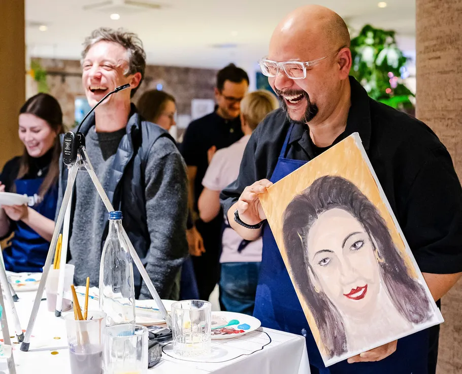 Zwei Personen lachen, halten ein Gemälde.