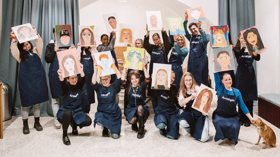 Group holding portrait paintings in art studio.