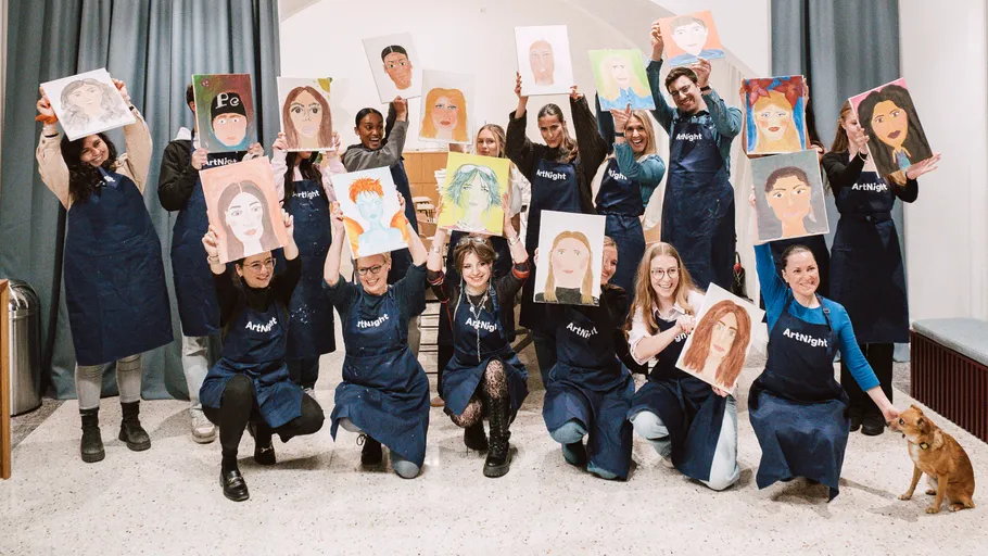 Group holding portrait paintings in art studio.