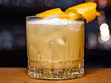 Glass with orange cocktail, bar background.