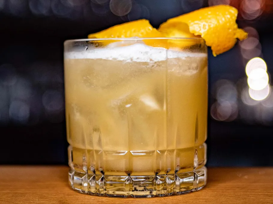 Glas mit orangem Cocktail, Barhintergrund.