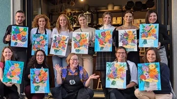 Group holding colorful paintings outdoors.