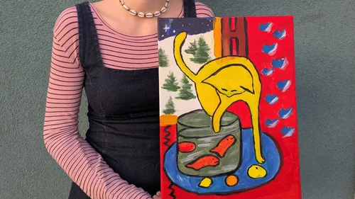 Person holding colorful cat painting outside.