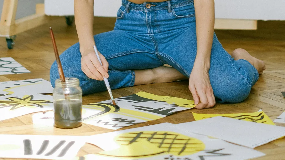 Person painting on floor with paper sketches.