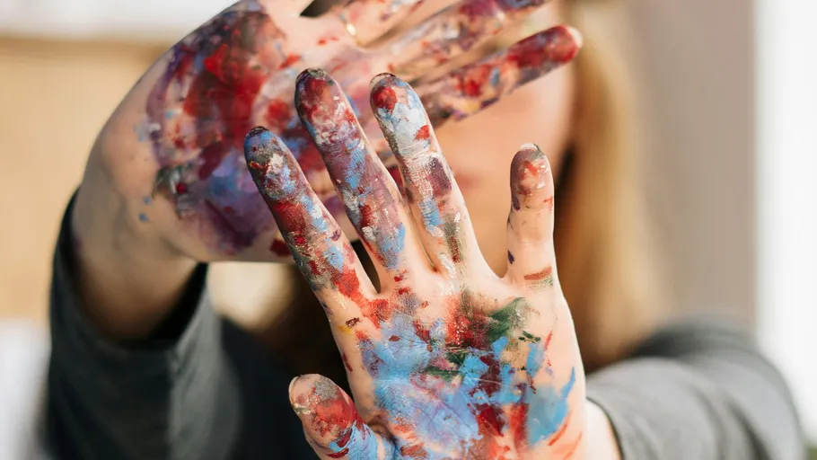 Hands covered in colorful paint outdoors.