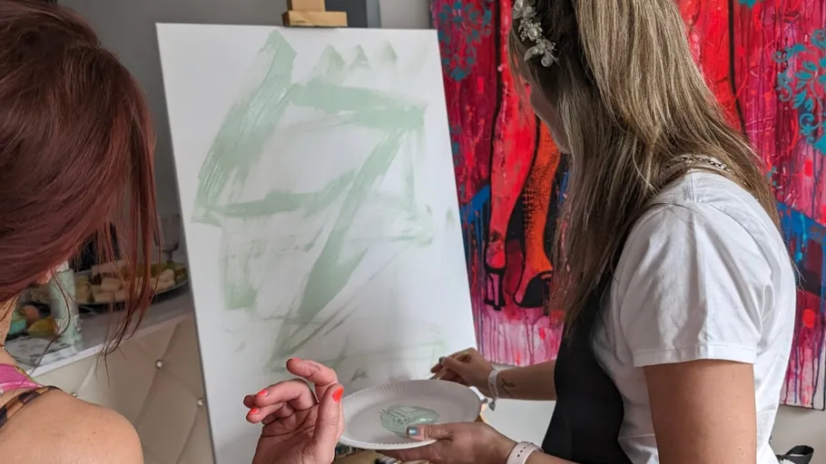 Two women painting on a canvas indoors.