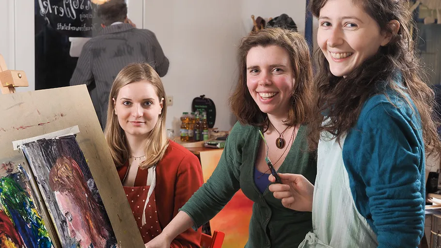 Three women smiling, painting together indoors.