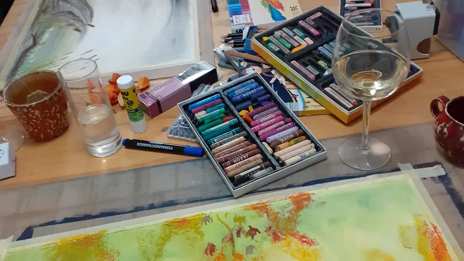 Art supplies on table with wine glass.