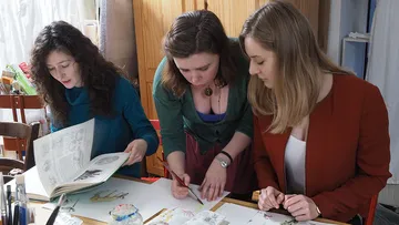 Drei Frauen arbeiten gemeinsam an Kunst am Tisch.