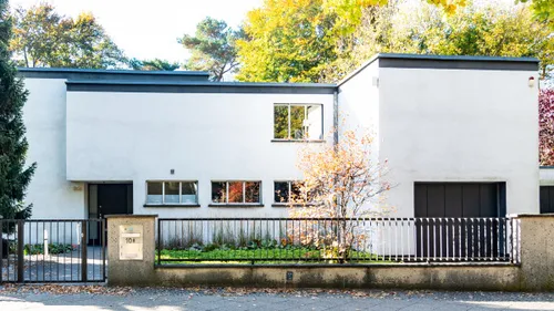 Modern white house with large windows, trees surrounding.