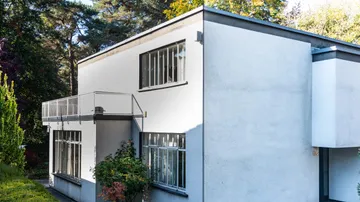 Modern white building with balcony in forest.