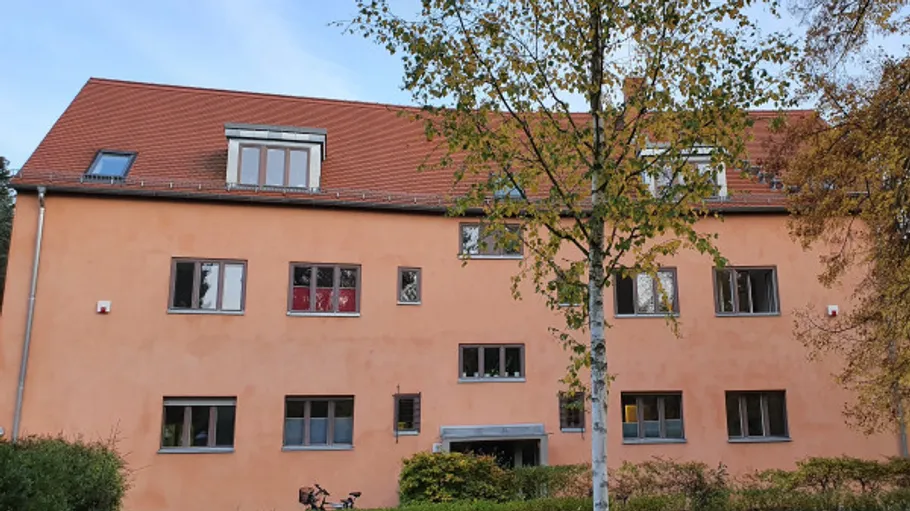 Zweistöckiges Gebäude mit orangefarbener Fassade, Baum vorne.