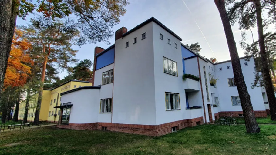 Modernist white building in wooded area.