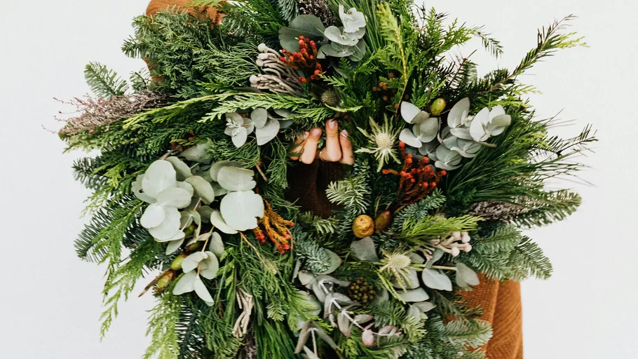 Person holding green wreath against white background.