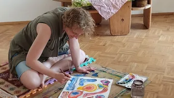 Person malt abstrakte Formen auf Papier im Innenraum.