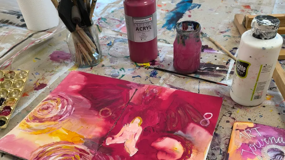 Kunsttagebuch mit Farben auf unordentlichem Tisch.