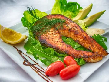 Grilled fish with salad and fresh vegetables on plate.