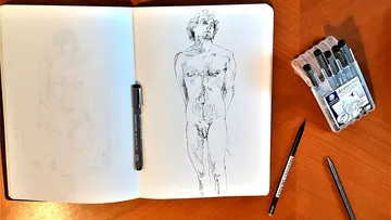 Skizzenbuch mit Menschenskizze, Stifte in der Nähe.