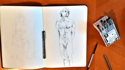 Skizzenbuch mit Menschenskizze, Stifte in der Nähe.