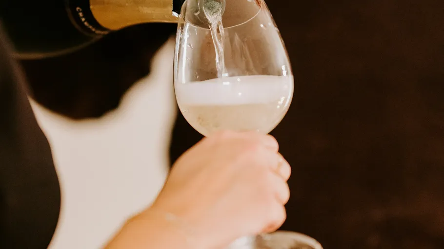 Hand gießt Champagner in ein Glas.
