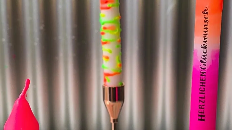 Bunte Kerze mit deutschem Text, metallischer Hintergrund.