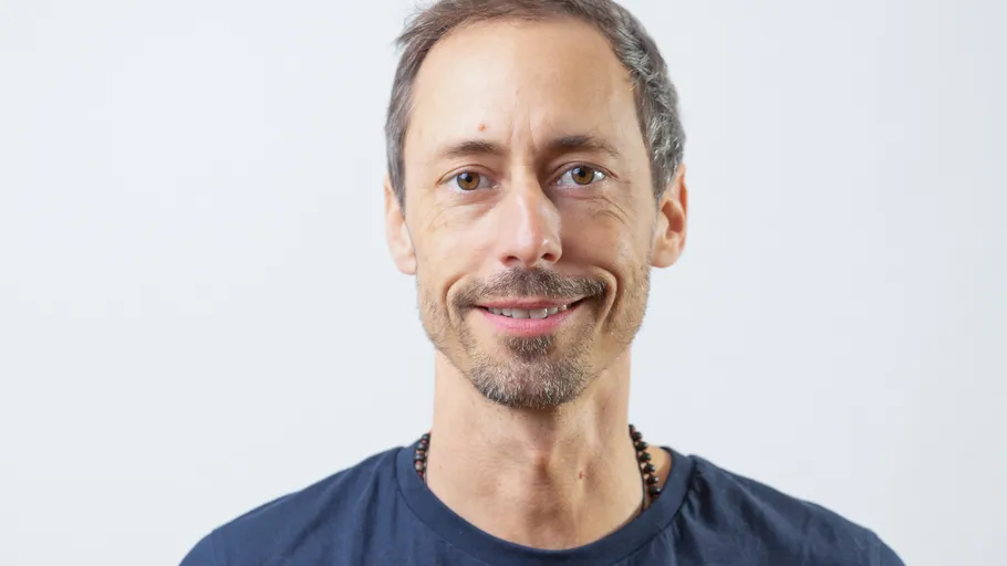 Lächelnder Mann mit kurzen Haaren vor schlichtem Hintergrund.