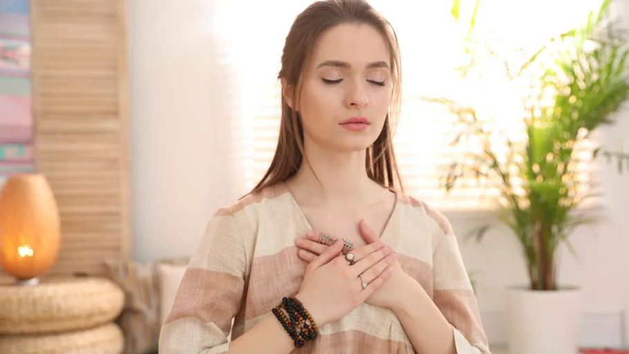 Woman meditating indoors with hands on chest.