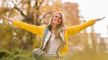 Smiling woman with arms raised outdoors.