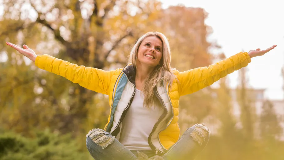 Smiling woman with arms raised outdoors.