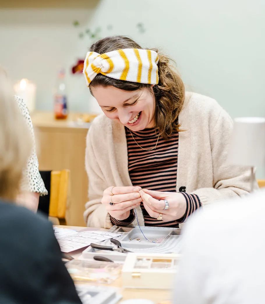 Woman crafting beads on table, smiling joyfully.