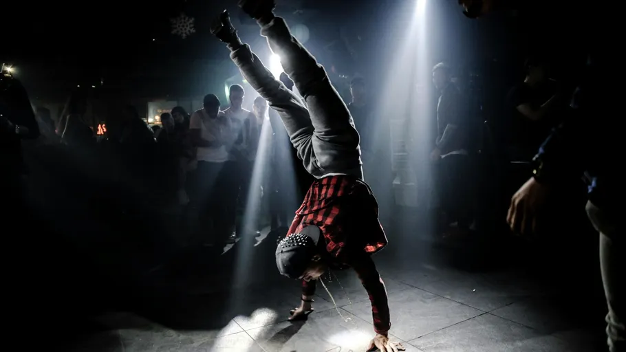 Dancer performs handstand under spotlight, crowd watches.