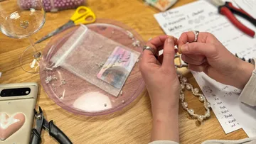 Hands making jewelry on a wooden table.