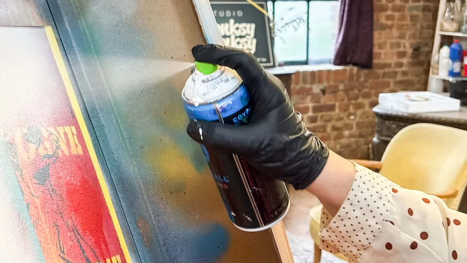 Hand spray-painting canvas in a studio.