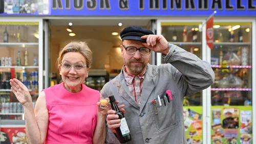 Zwei Personen lächeln vor einem Kiosk.