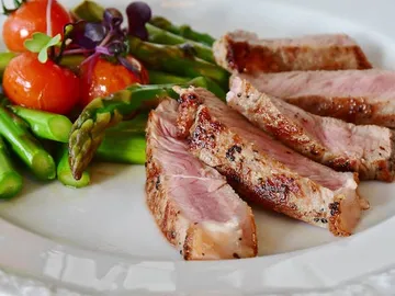 Grilled meat sits next to asparagus and cherry tomatoes.
