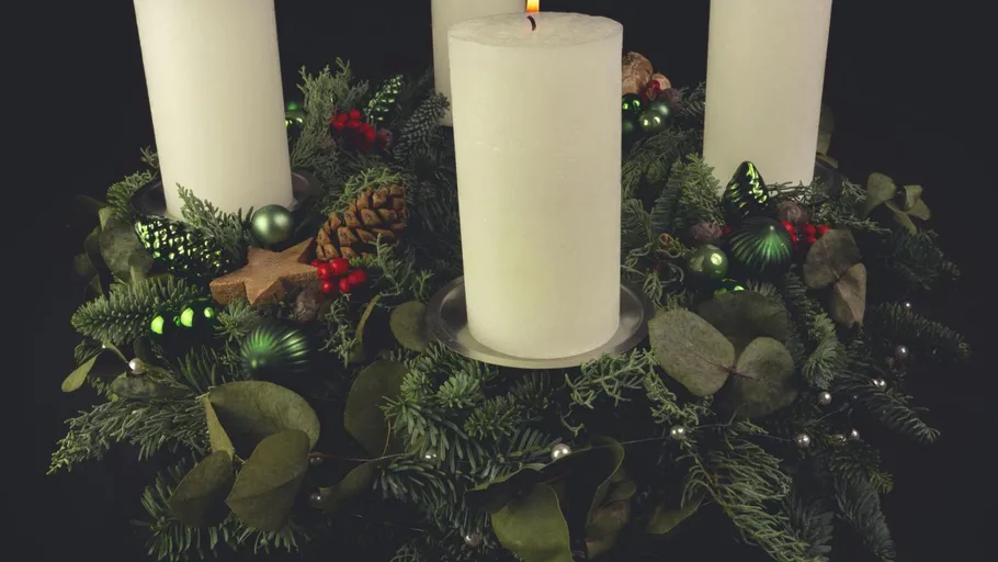 Kerze auf Adventskranz mit Weihnachtsdekoration.