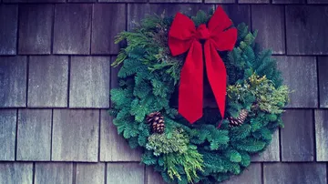 Weihnachtskranz mit roter Schleife an Wand.